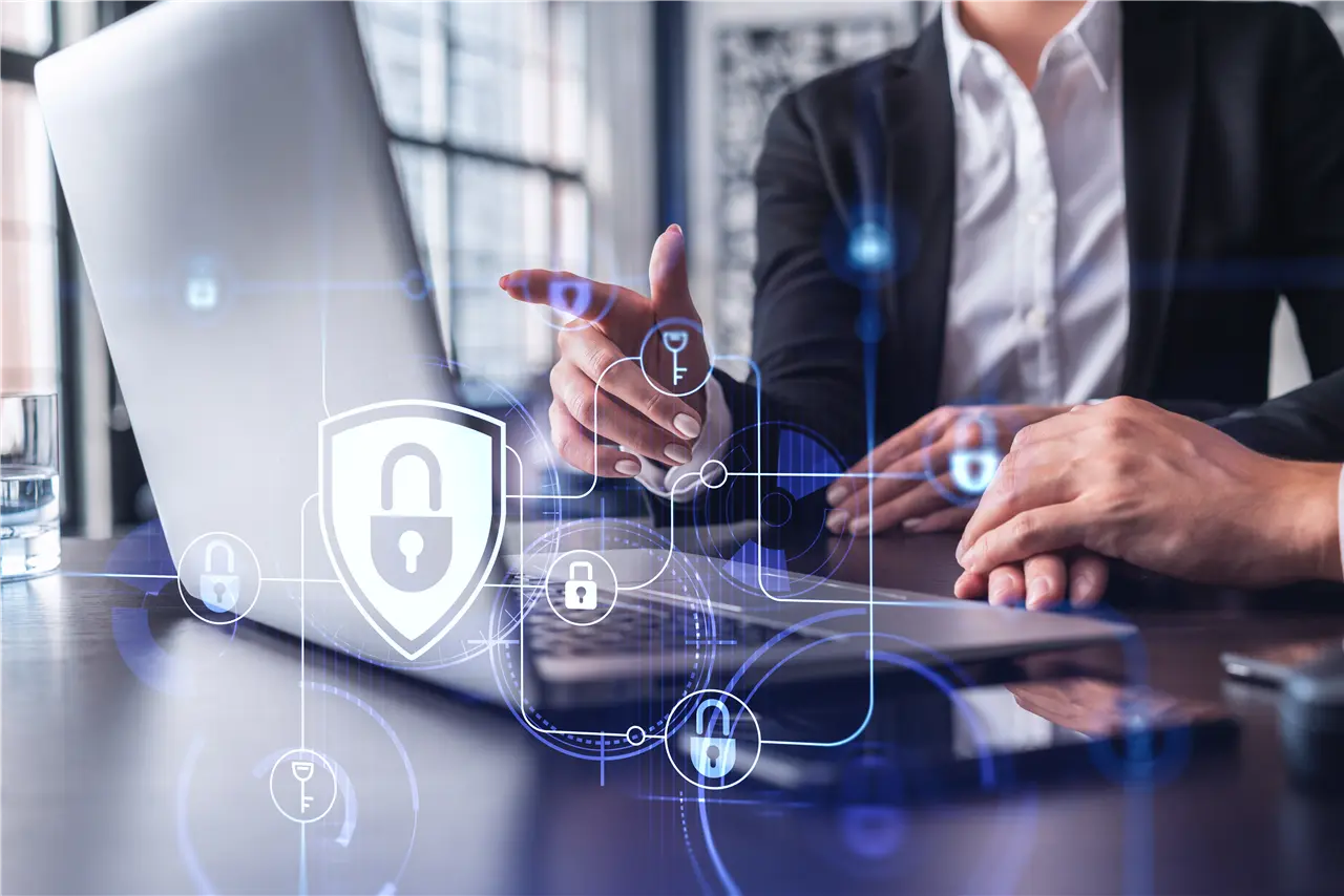 Eine Person zeigt auf einen Laptop in einem modernen B&uuml;ro. Es gibt digitale Symbole von Schl&ouml;ssern und Schl&uuml;sseln, die Datensicherheit darstellen.