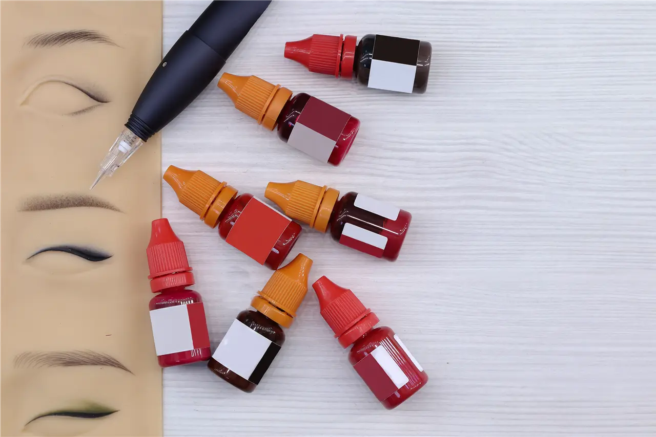 Die Grafik zeigt eine Sammlung von Farbtintenflaschen und ein Pigmentierger&auml;t auf einem Tisch, zusammen mit einer &Uuml;bungshaut mit Augen- und Augenbrauenmotiven.