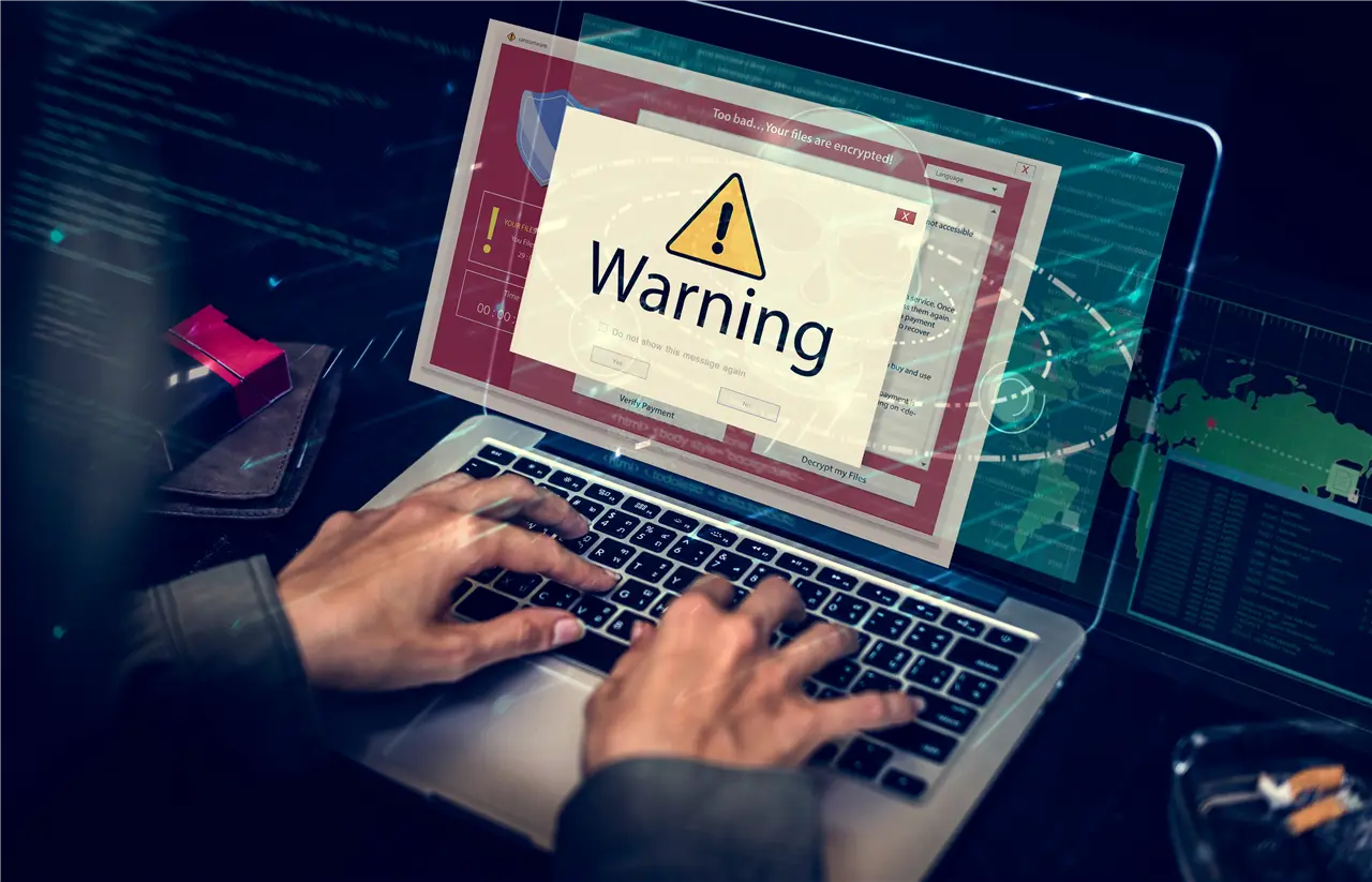 Ein Computerbildschirm zeigt eine Warnmeldung an, w&auml;hrend eine Person daran arbeitet. Der Bildschirm ist von einem roten Rahmen umgeben, was auf ein m&ouml;gliches Sicherheitsproblem hinweist. Die H&auml;nde der Person sind sichtbar, die eine Tastatur bedient.