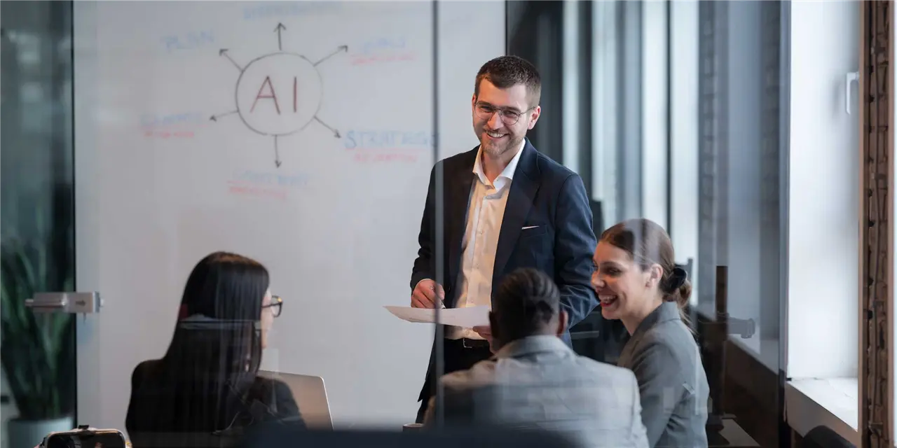 Meeting in einem Seminarraum mit vier Personen, im Hintergrund ist ein Whiteboard zu sehen mit Grafiken zum Thema KI.